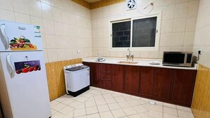 Cocina compacta con refrigerador, lavadora, microondas y ventana con reloj.