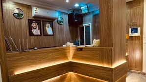 Un mostrador de recepción con detalles de madera e iluminación integrada, un reloj y retratos enmarcados en la pared.