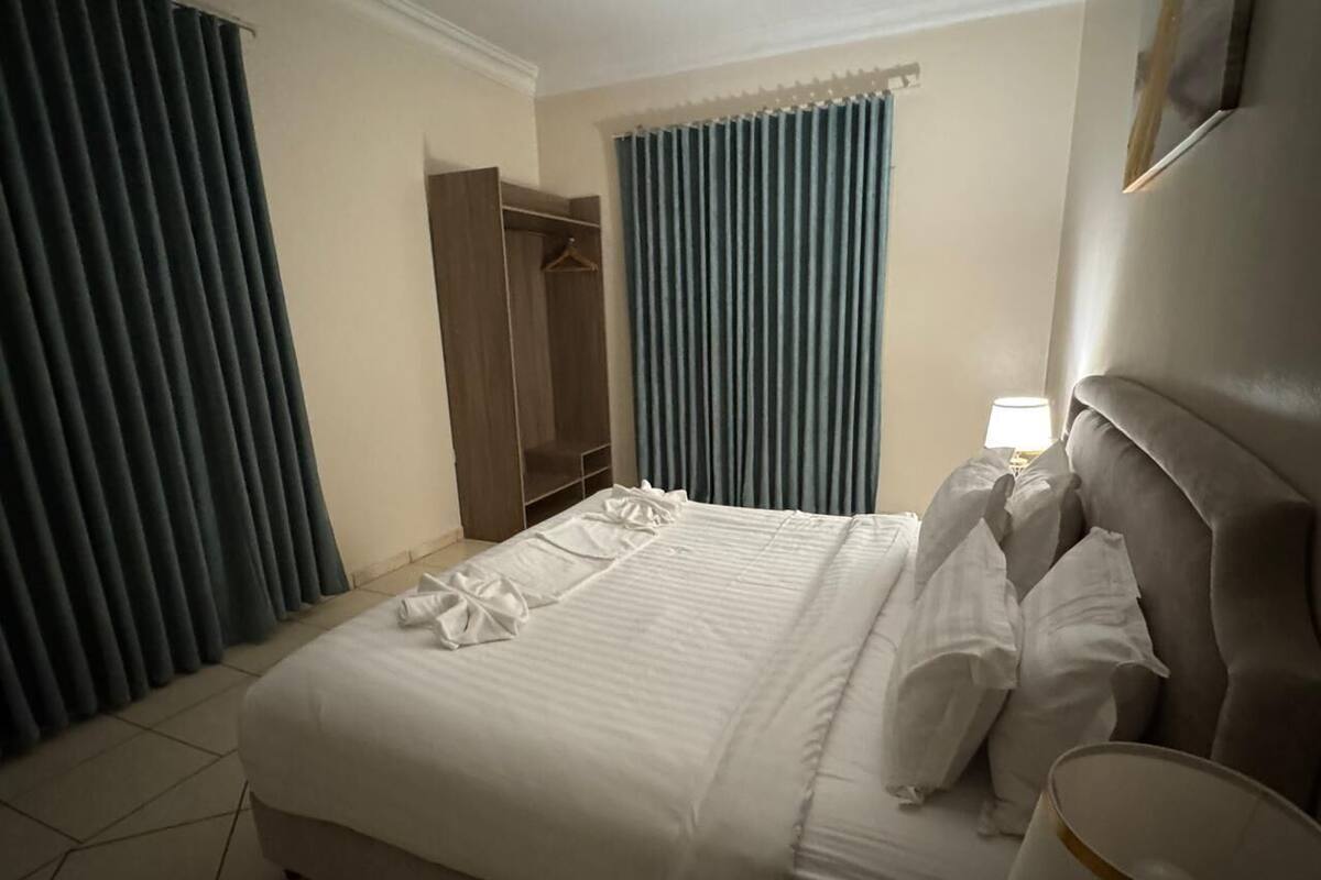 Une chambre d’hôtel avec un grand lit, une armoire, une table de chevet avec une lampe et une fenêtre avec des rideaux.