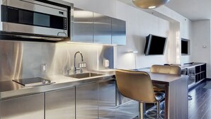 A modern kitchen with stainless steel appliances, a bar area with stools, and a flat-screen TV mounted on the wall.