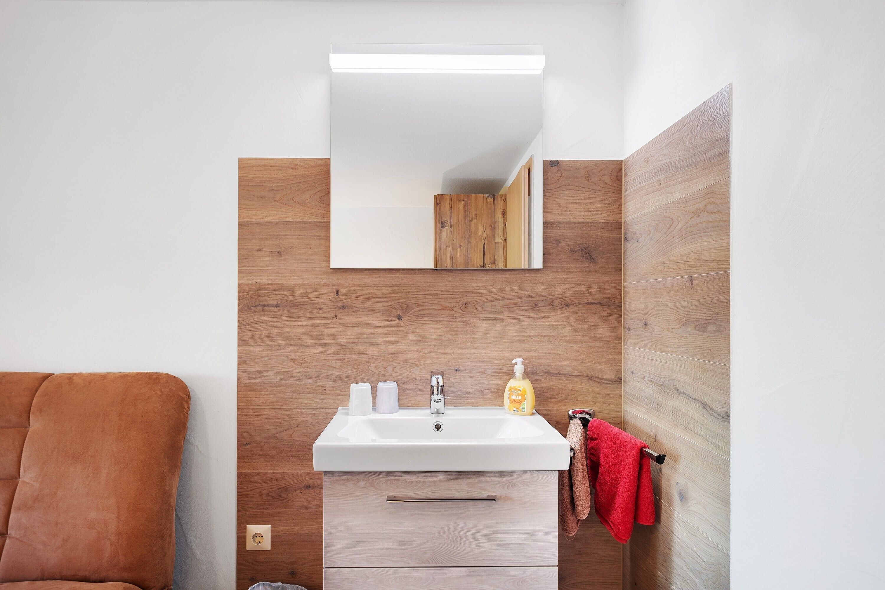 A bathroom with a white sink, wooden wall paneling, a mirror, and a red towel.