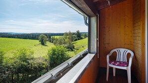 A room with a view of a green field and trees, a white plastic chair, and wooden walls.