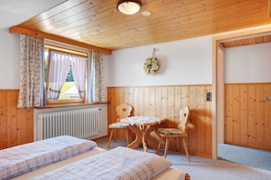 A wooden-paneled room with two beds, a table with chairs, a radiator, and a window with curtains. - Apartment 'Feldbergblick' with Mountain View, Shared Garden and Wi-Fi (Furtwangen)