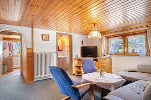 A cozy room with a wooden ceiling, a television, a sofa, a table with a floral tablecloth, and a window with curtains. - Apartment 'Feldbergblick' with Mountain View, Shared Garden and Wi-Fi (Furtwangen)
