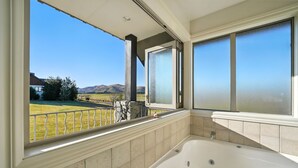 Un baño con bañera, vista a un jardín con césped y una pared de piedra.