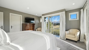 Un dormitorio con una cama grande, un televisor en una cómoda, una silla y un balcón con vistas a la montaña.