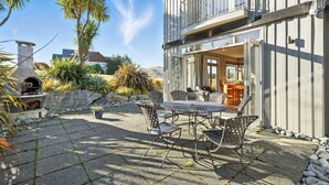 Un patio con mobiliario exterior, una chimenea de piedra y vista a una casa con balcón.