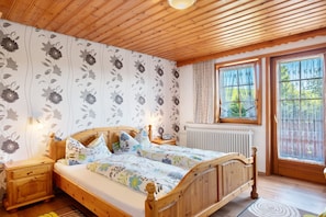 A wooden bed with floral bedding, a nightstand, a bedside table, a window with curtains, and a radiator.