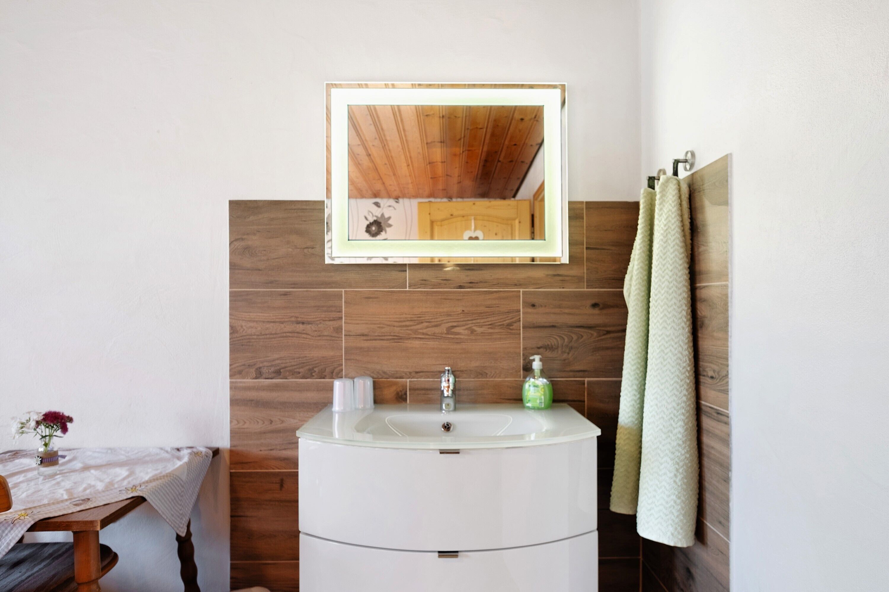 A bathroom with a wooden wall, a white sink, a mirror, and a towel rack.