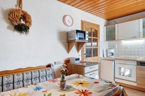 A cozy kitchen with wooden cabinets, a microwave, a refrigerator, and a dining area with a floral tablecloth.