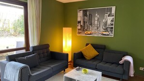 A living room with two grey sofas, a coffee table, a floor lamp, and a cityscape painting on the wall. - Apartment 'Heinrich' with Private Terrace, Garden, and Wi-Fi (Schramberg)