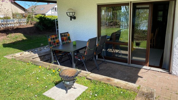 A patio with a table and chairs, a grill, and a sliding glass door to a garden. - Apartment 'Heinrich' with Private Terrace, Garden, and Wi-Fi (Schramberg)