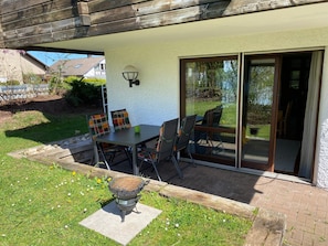 Eine Terrasse mit Tisch, Stühlen, einem Grill und einer Glastür zum Garten.