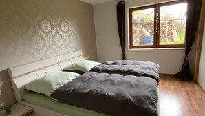 A bedroom with a bed, wooden flooring, a nightstand, a window with curtains, and a ceiling light fixture. - Apartment 'Heinrich' with Private Terrace, Garden, and Wi-Fi (Schramberg)