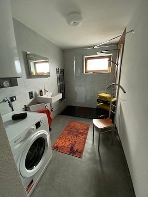 Ein kleines Badezimmer mit Waschmaschine, Waschbecken, Spiegel und Fenster.
