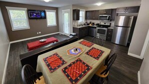 Una cocina moderna con comedor, equipada con electrodomésticos de acero inoxidable, un televisor de pantalla plana y una isla grande con mantel estampado en rojo y negro.