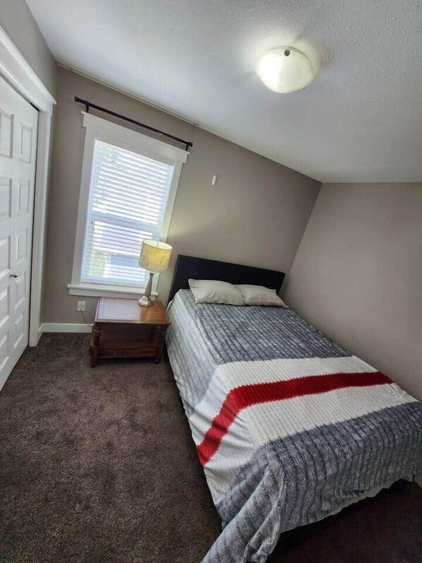 A bedroom with a bed, a nightstand, a lamp, and a window with blinds. - Elegant Family House by  Stadium, Airport,Shopping (Regina)