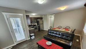 Un espacio habitable compacto con kitchenette, zona de comedor con mesa y sillas, y un sofá de cuero negro.