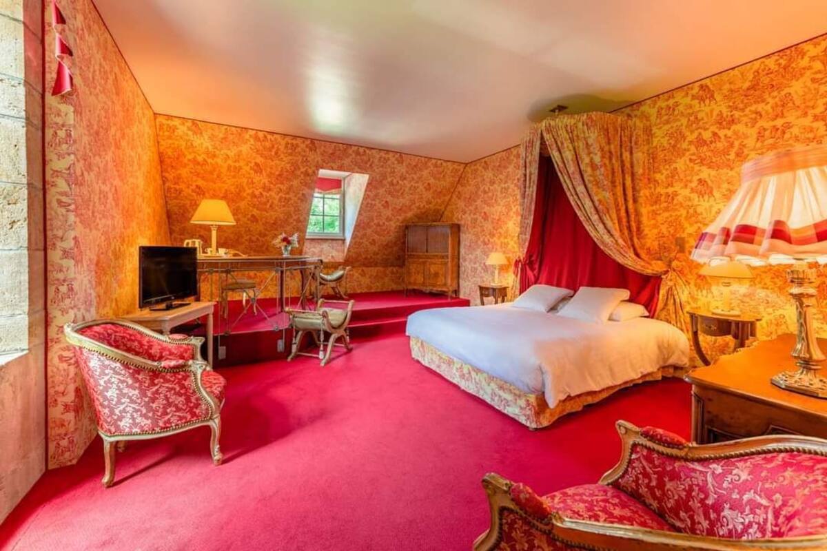 A hotel room with a large bed, two armchairs, a desk with a computer, and a TV.