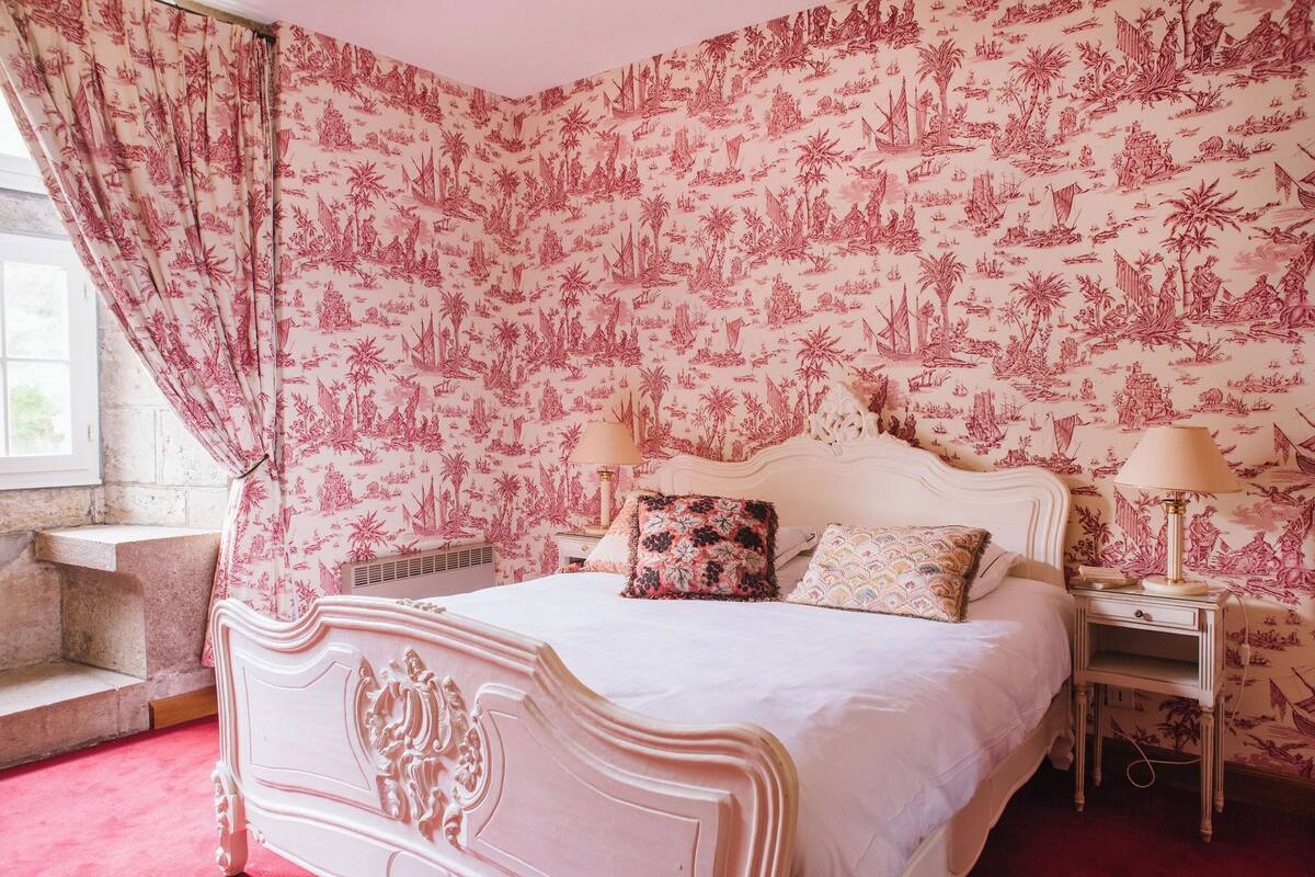 A bedroom with a bed, two bedside tables, a window, and a patterned wallpaper.