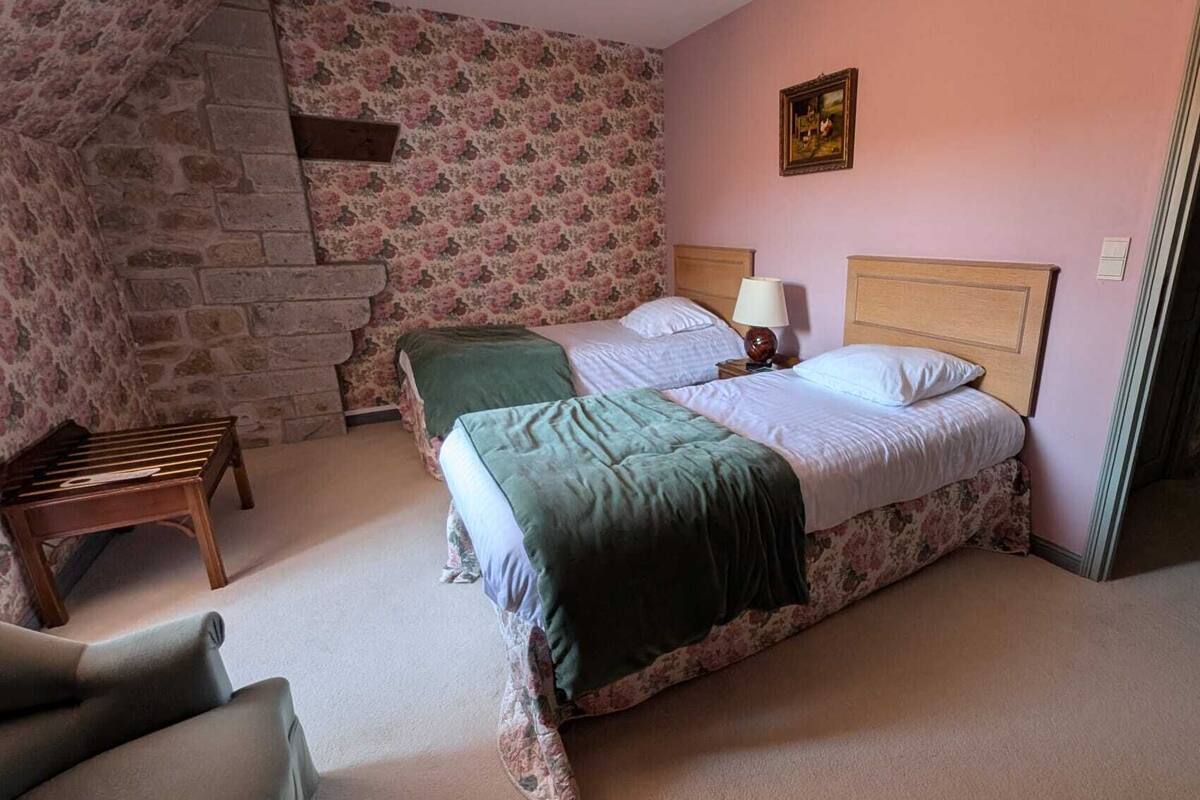 A bedroom with two beds, a wooden bench, a stone wall, and a framed picture on the wall.