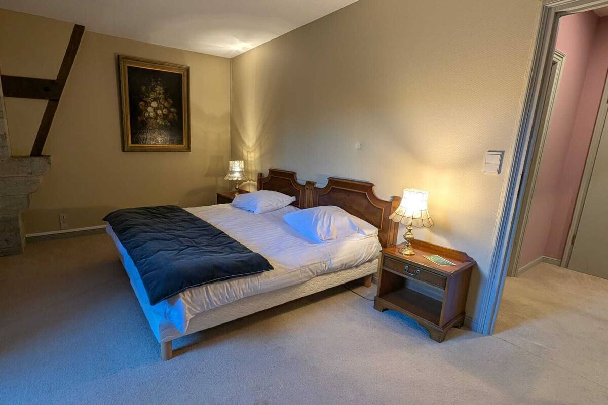 A bedroom with a bed, two bedside tables, a lamp, a painting, and a stone wall.