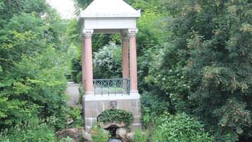 Een stenen kiosk met zuilen en een dak, omgeven door weelderige begroeiing en een kleine waterval.