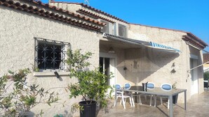 Ein Gebäude mit einem Ziegeldach, einem Fenster mit Metallgitter und einer Terrasse mit Tisch und Stühlen.