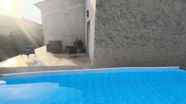 Ein Schwimmbecken mit klar blauem Wasser, umgeben von einer Betonplattform und einer Steinmauer.
