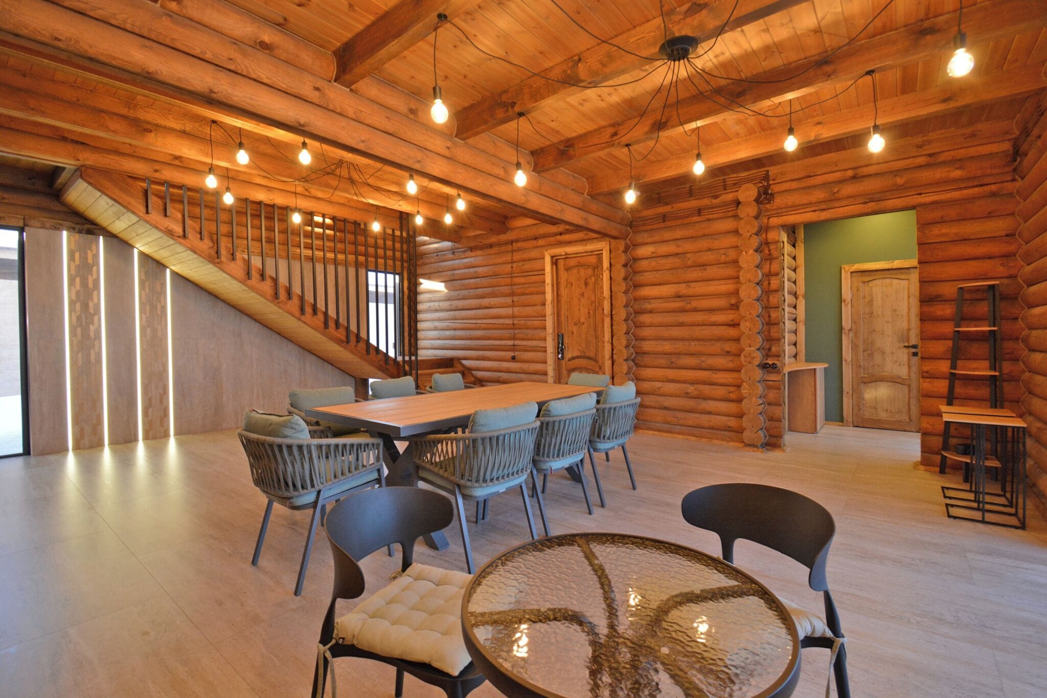 A log cabin interior with a dining area, chairs, a table, a staircase, and a ladder.