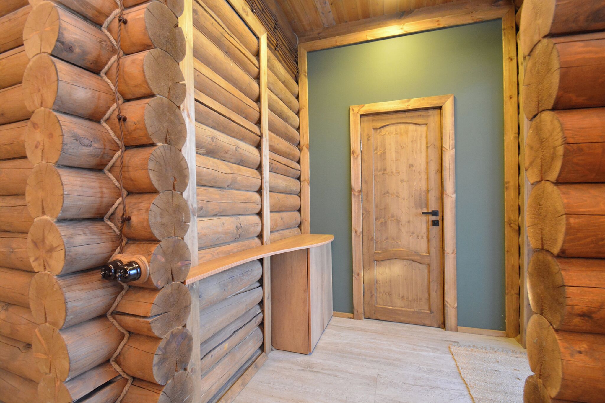 A log cabin interior with a wooden door, a bench, and a light-colored floor.