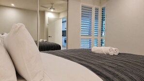Una habitación de hotel con una cama, un espejo grande y vistas al exterior a través de una ventana con persianas.