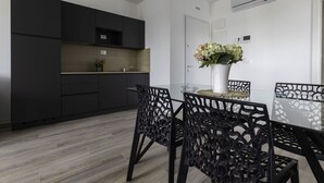 A modern kitchen with dark cabinets, a white countertop, and a glass dining table with black chairs. - Enjoy our Studio With Terrace in Bibione (San Michele al Tagliamento)