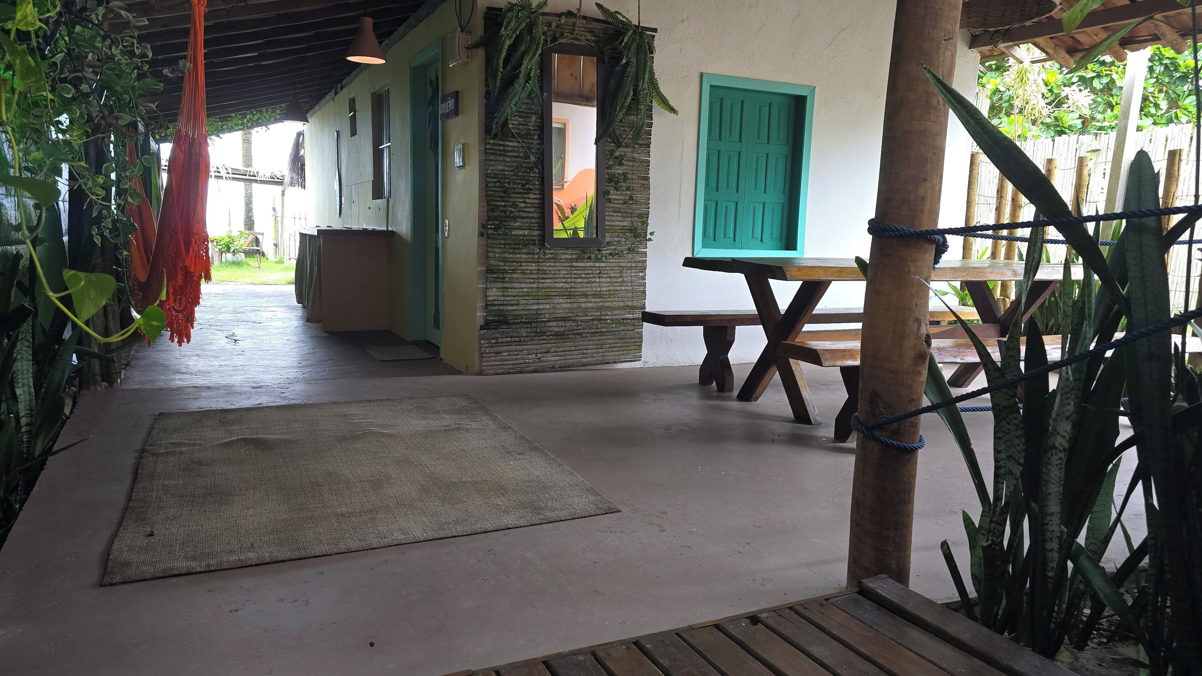 A covered outdoor area with a wooden table, a bench, and a hanging hammock.