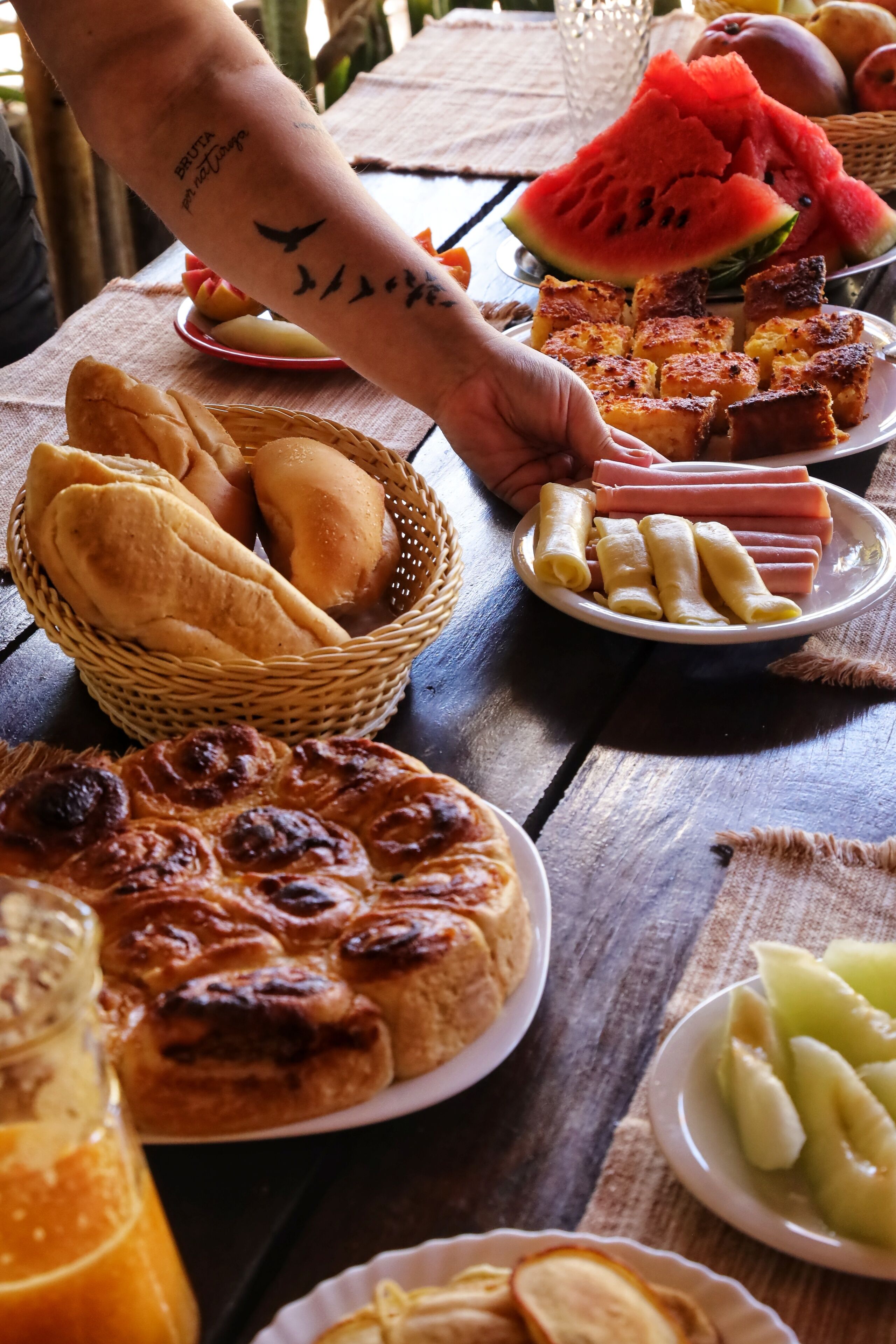 Un tavolo con diversi cibi, tra cui pane, panini e una fetta di anguria.