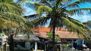 Un paisaje tropical con una cabaña de techo de paja, una palmera y una zona vallada.