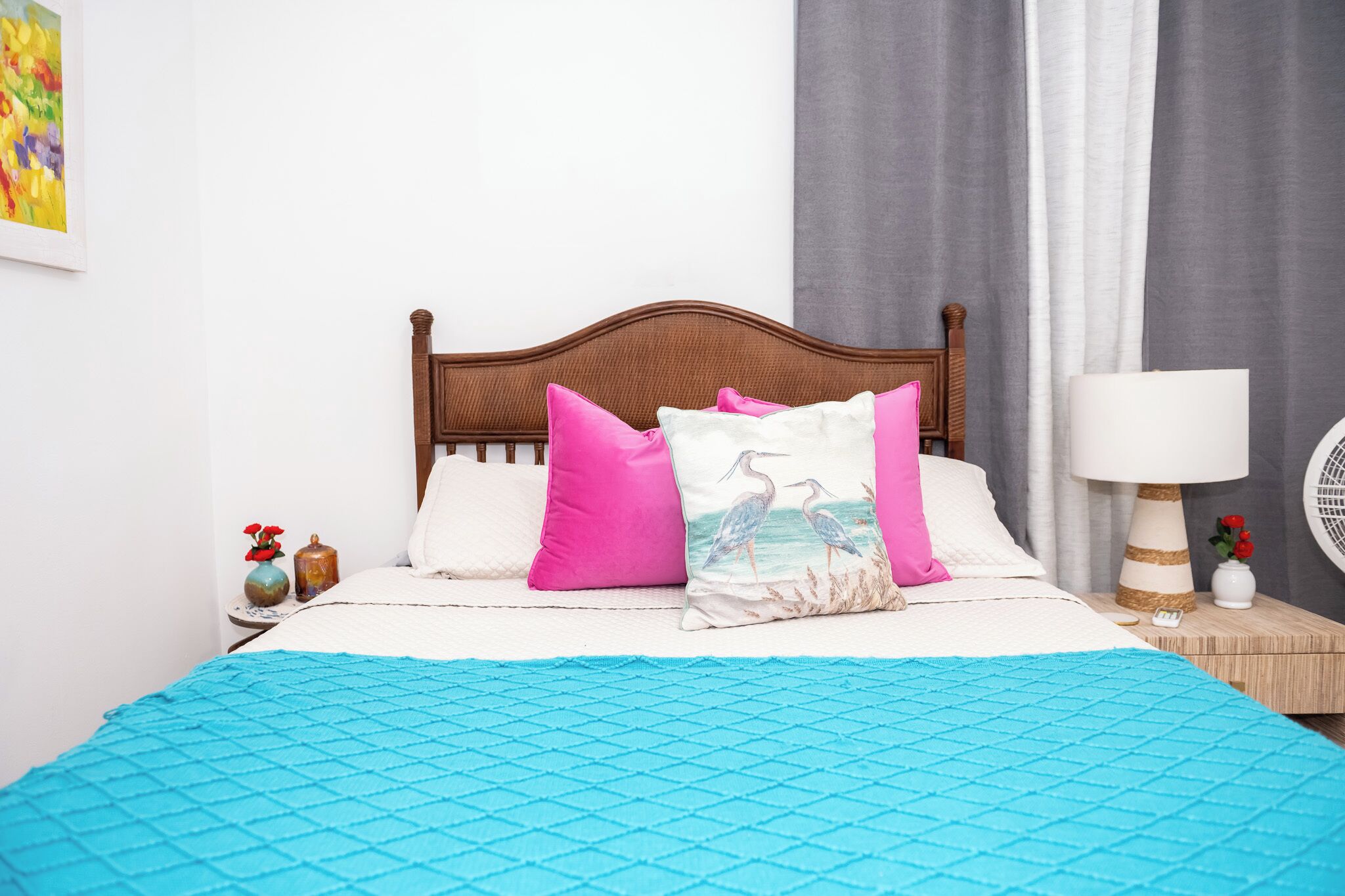 En snyggt bäddad säng med ett blått täcke, en trägavel och rosa och vita kuddar.