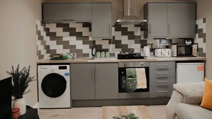 A compact kitchen with grey cabinets, a microwave, a toaster, and a washing machine. - 1BR Retreat l Great Value (West Midlands)