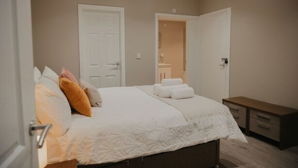 A bedroom with a bed, two doors, a bedside table, and a wooden bench. - 1BR Retreat l Great Value (West Midlands)