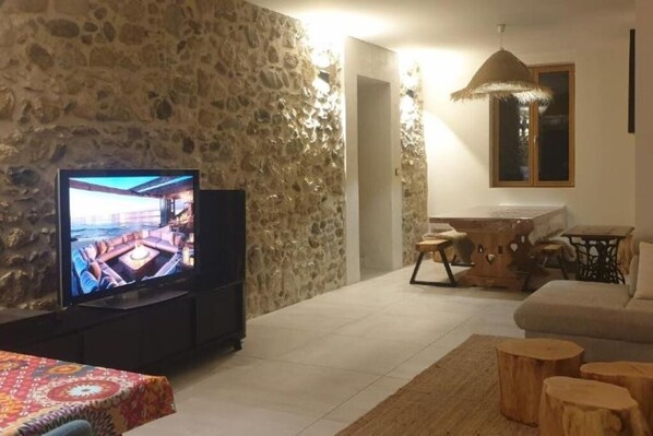 A living room with a stone wall, a television, a sofa, and a dining area with a table and chairs.