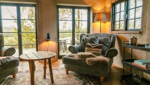 A cozy living room with a large window, a comfortable armchair, a small table, and a lamp. - Cottage "Am Wald" rechts (Bissee)