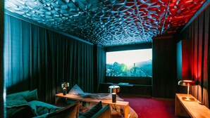 A modern room with a unique geometric ceiling, a large window with a mountain view, a cozy seating area with cushions, and a small table with a lamp. - Cottage "Am Wald" rechts (Bissee)