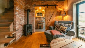 A cozy living room with a brick fireplace, wooden staircase, and a comfortable seating area with a view of the outdoors. - Cottage "Am Wald" rechts (Bissee)
