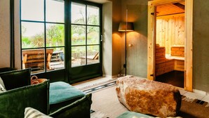 Una habitación acogedora con un amplio ventanal corredero que da a un espacio exterior, una sauna de madera y un área de descanso confortable con cojines.