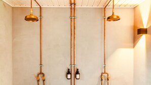 Un baño con tuberías de cobre, dos cabezales de ducha y una lámpara empotrada en la pared.