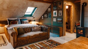 Un dormitorio tipo loft acogedor, con techo inclinado, una cama grande, un sofá de cuero y un suelo de madera rústica.