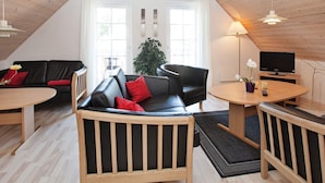 A cozy loft-style living room with a high ceiling, a black leather sofa, a wooden coffee table, and a television on a wooden stand. - 8 Person Holiday Home on a Holiday Park in Grasten (Grasten)