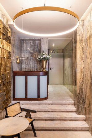 A reception area with a marble wall, a wooden reception desk, a vase with flowers, and a staircase leading to another room.
