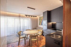 Una cocina moderna con horno empotrado, una zona de comedor con mesa redonda y sillas, y un ventanal con cortinas ligeras.