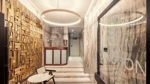 A modern lobby with a reception desk, a seating area with a round table, and a marble wall.